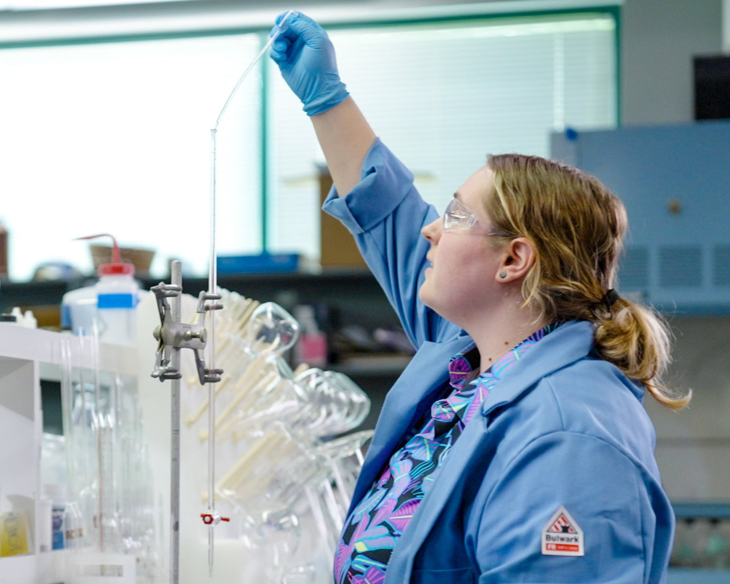 Person in a laboratory wearing a blue lab coat and gloves, working with equipment.